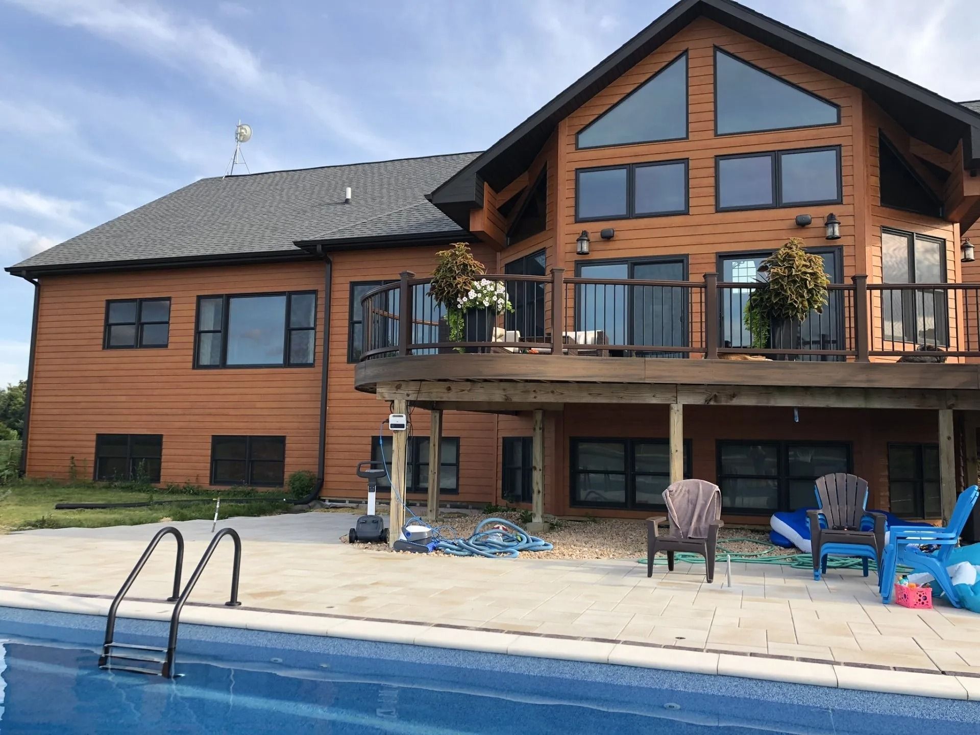 Brown house with pool, wooden deck, and large windows on a sunny day.