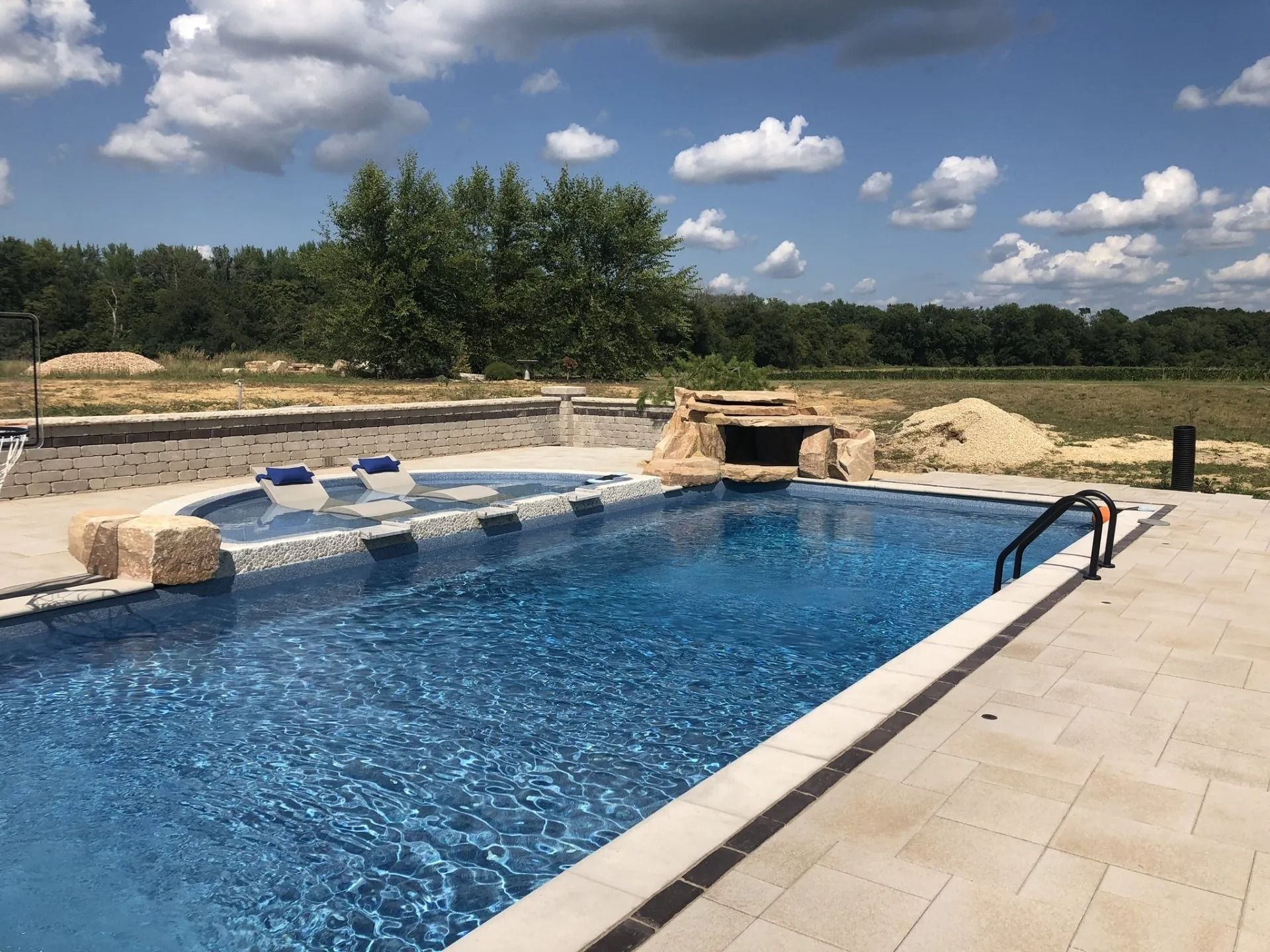 Pool with blue water, stone features, and a lush green background under a blue sky.