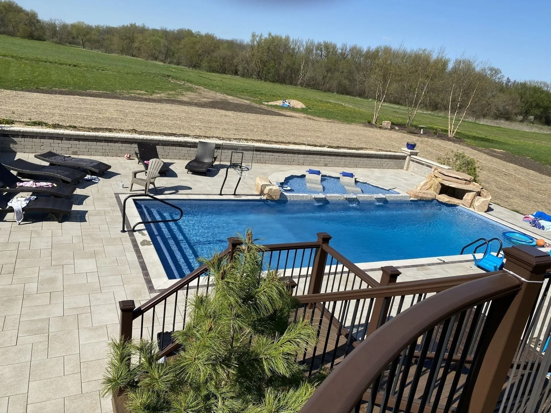 Outdoor swimming pool with lounge chairs, overlooking a grassy hill on a sunny day.
