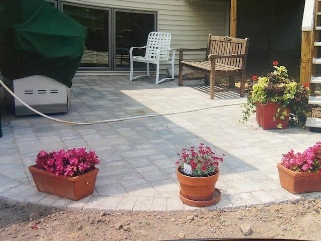 A patio with flower pots, chairs, and a grill under a green cover.