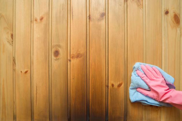 Pink-gloved hand wiping a wooden wall with a blue cloth