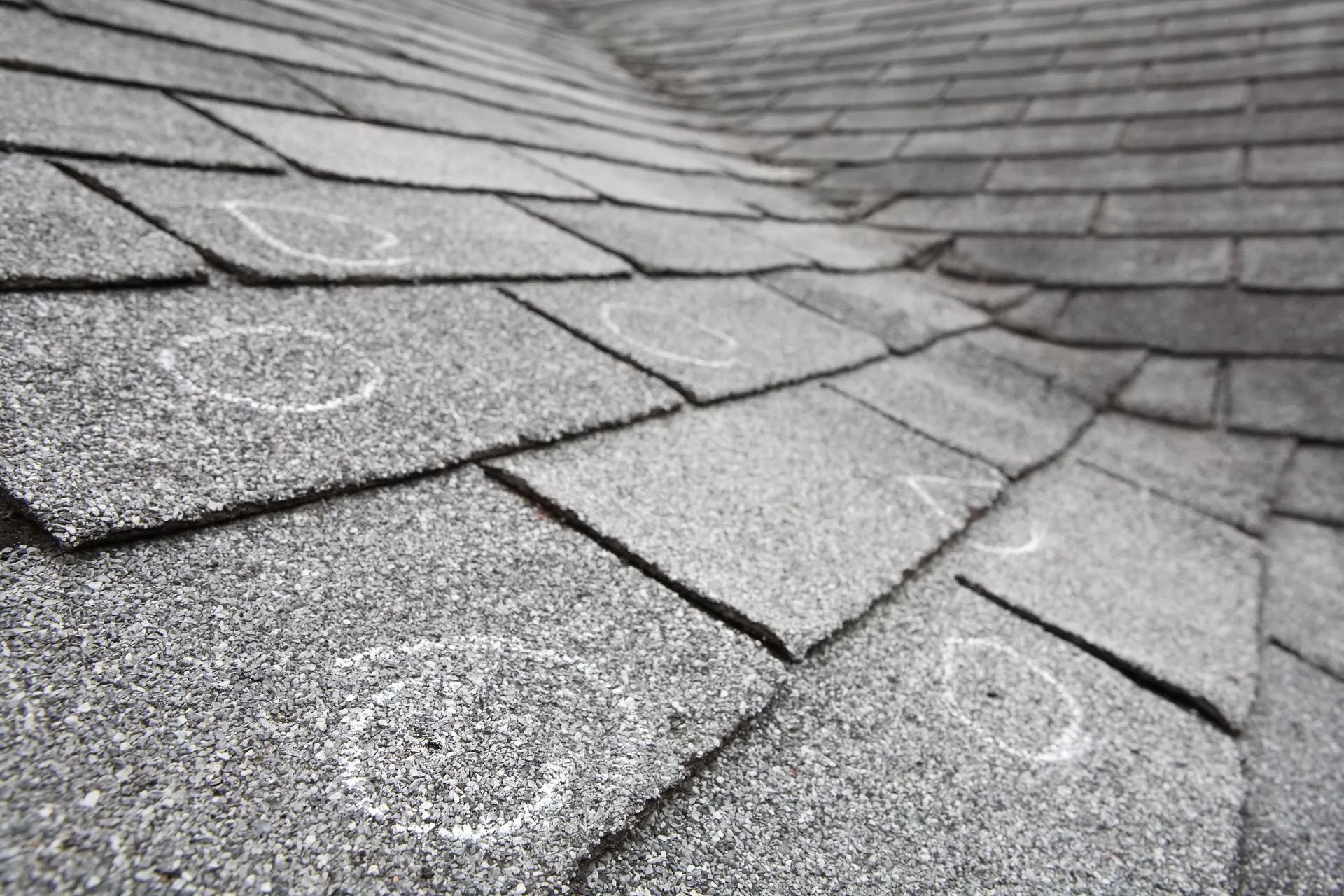Close-up of gray asphalt roof shingles with visible wear and chalk marks