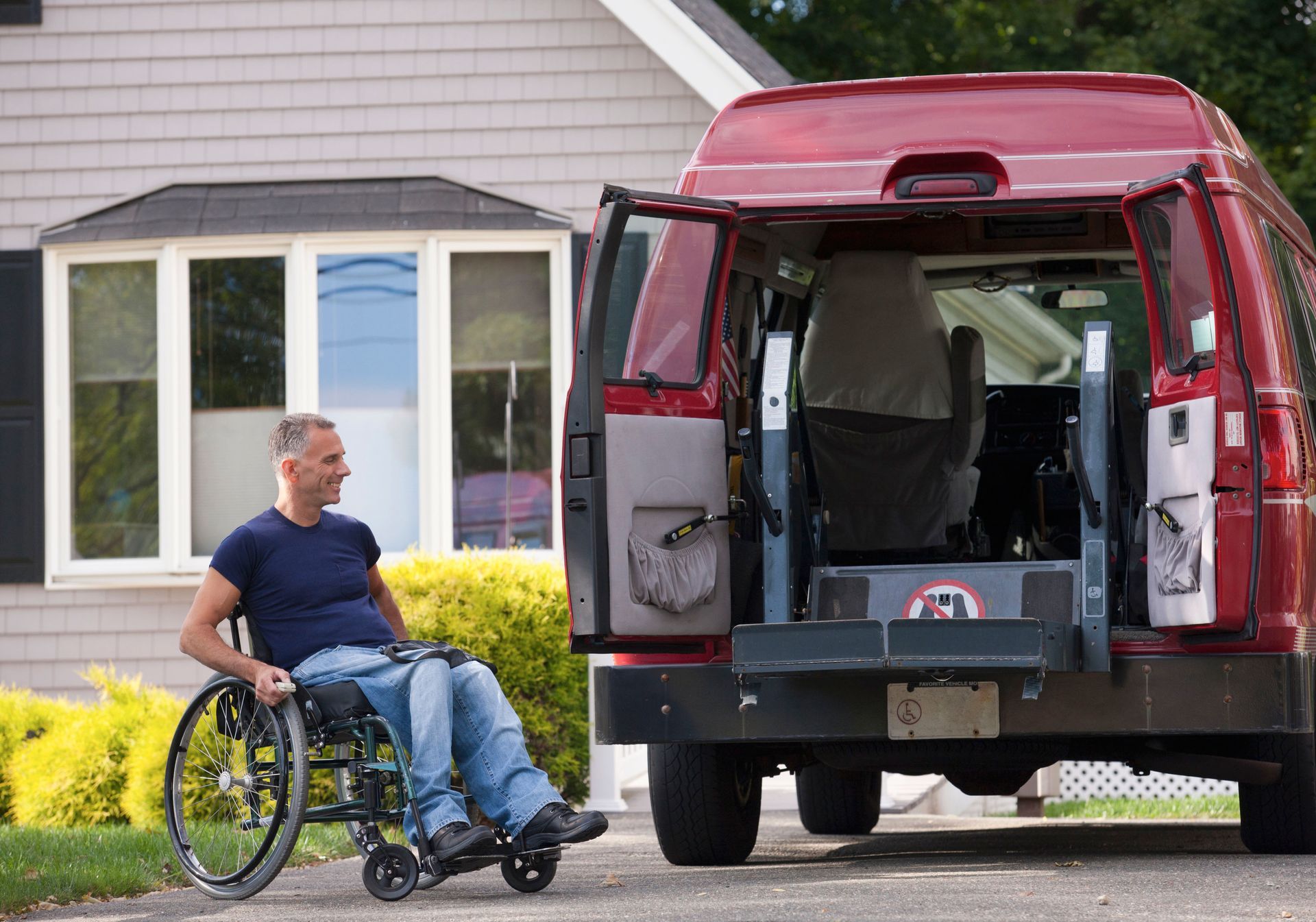 Man in wheelchair beside accessible van with open ramp.