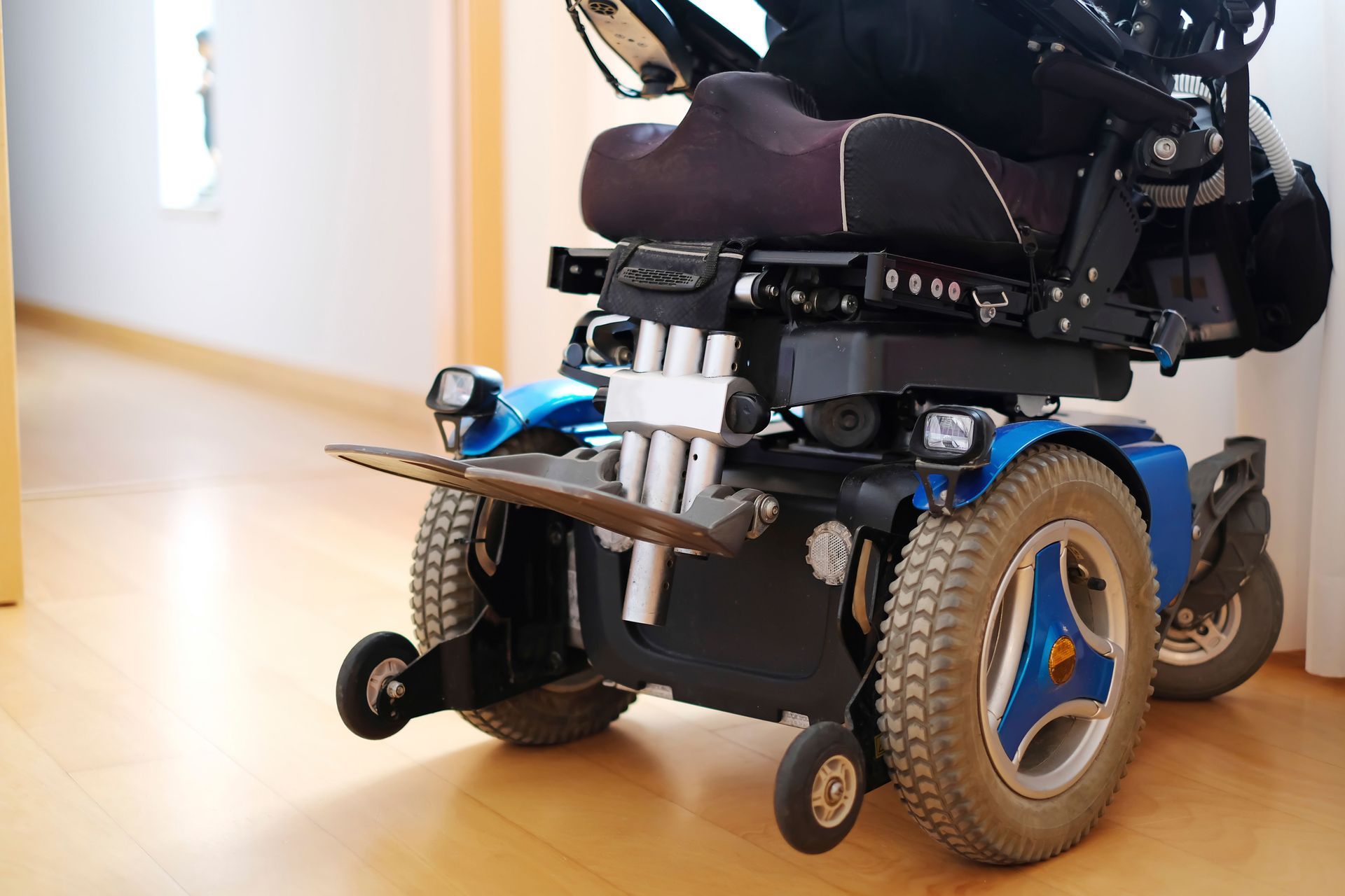 Blue and black power wheelchair in a room with light wood floors.