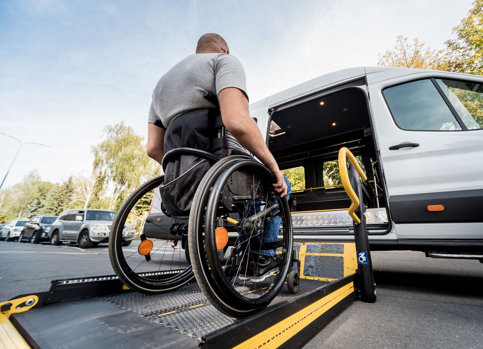 Person in wheelchair using a ramp to enter a white accessible van on a sunny day.