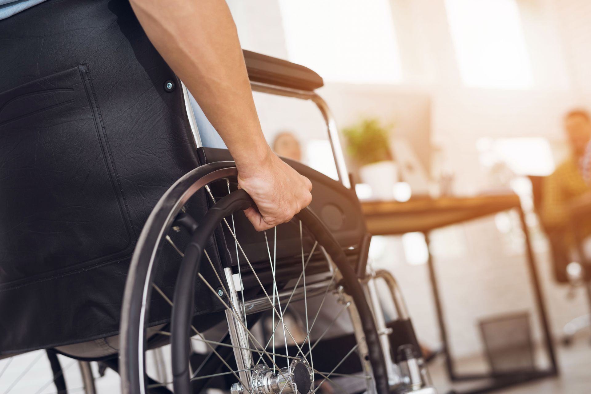 Person in a wheelchair at an office desk, gripping the wheel.