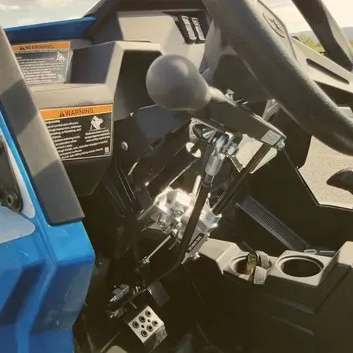 Interior view of a blue and black UTV. Shows the shift lever, pedals, and steering wheel.