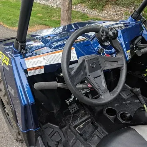 Interior of a blue UTV with black steering wheel, gear shift, and cup holders. Warning label visible.
