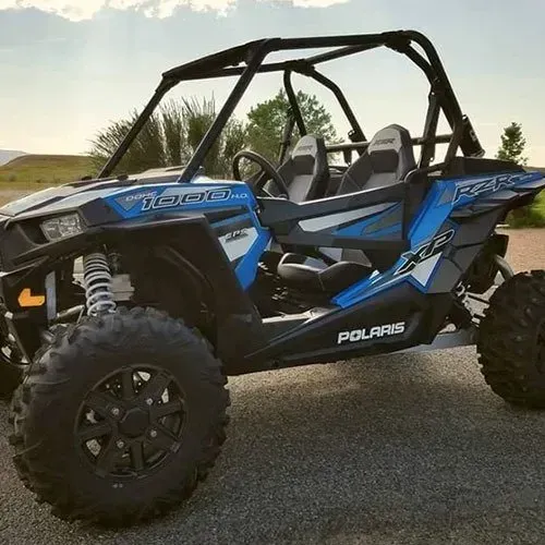 Blue and black Polaris RZR off-road vehicle with roll cage, parked outside.