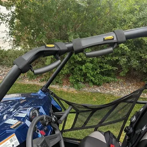Close-up of a UTV roll cage with black grab handles and straps attached to the bar.