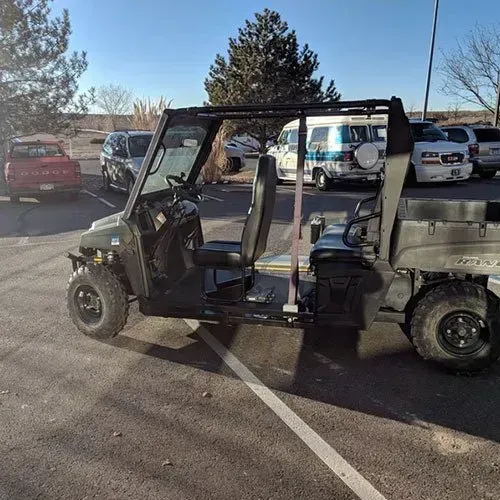 Green utility vehicle parked in a lot, with other vehicles in the background. Sunny day.