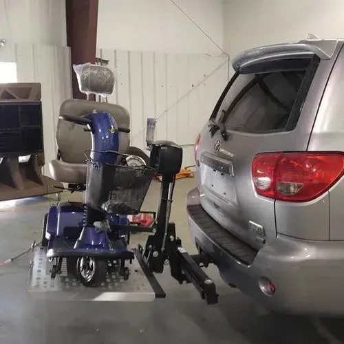 Blue mobility scooter on a platform next to a silver SUV, connected by a hitch-mounted lift.