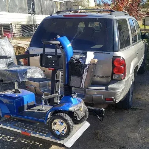 Blue mobility scooter on a ramp, being loaded into a silver SUV. Outdoors, sunny.
