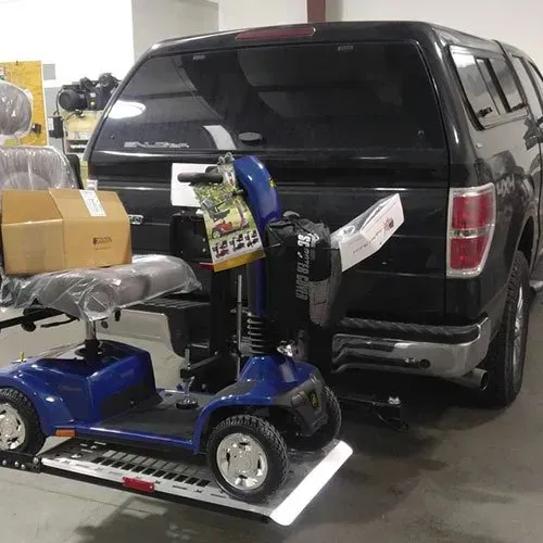 Blue mobility scooter on a ramp attached to the back of a black truck.