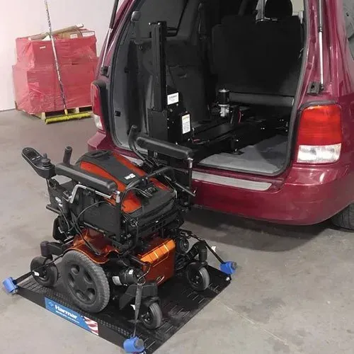 Power wheelchair on a ramp next to a modified minivan for accessibility.