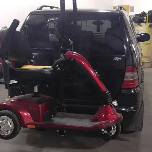 Red mobility scooter hitched to the back of a black SUV.