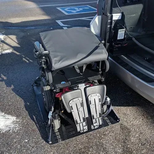 Wheelchair on a platform lift next to a vehicle, in a parking space.