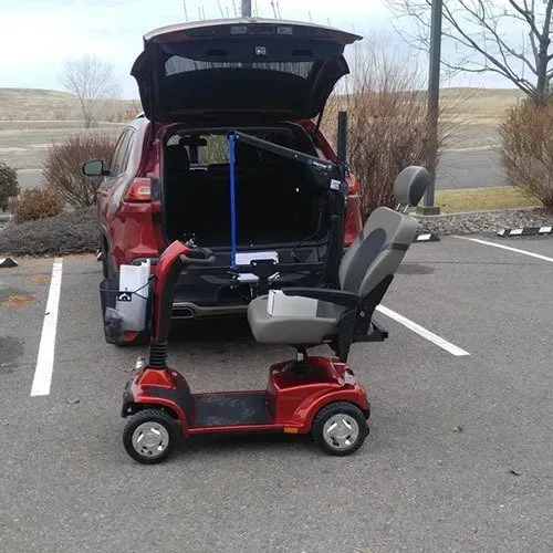 Red mobility scooter next to a red SUV with a lift. Parked in a parking lot.
