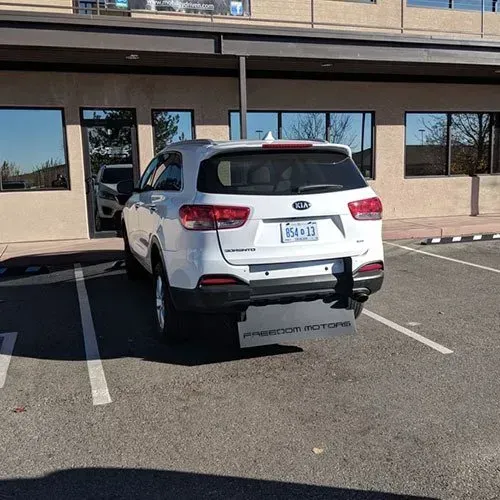 White Kia SUV parked outside a building with tinted windows;