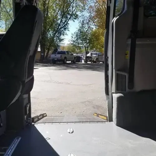View from inside a van towards an open door, with a parking lot and trucks visible outside.