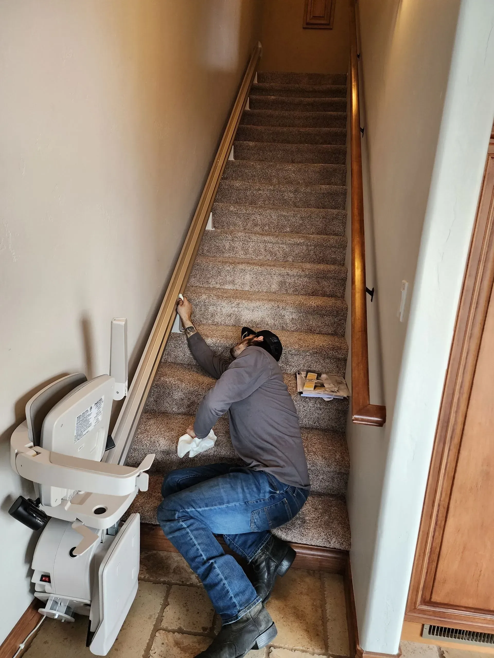 Person installing a stair lift on a staircase. Interior setting, person in jeans and long sleeve shirt.