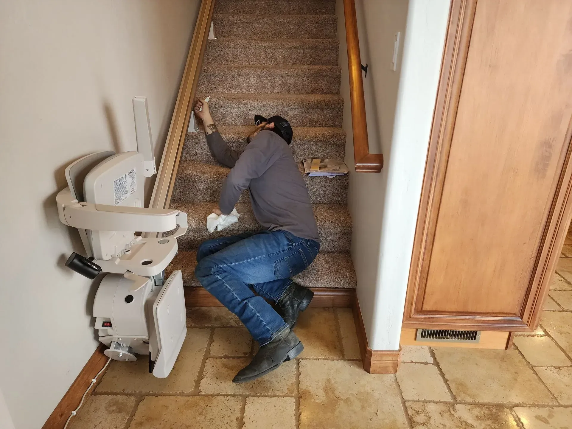 Person lies on stairs near stair lift; brown carpet, beige walls, wood cabinet.