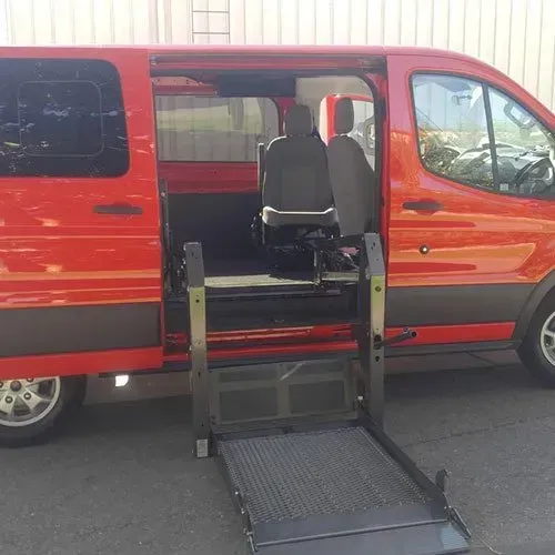 Red accessible van with wheelchair lift deployed, parked outdoors.