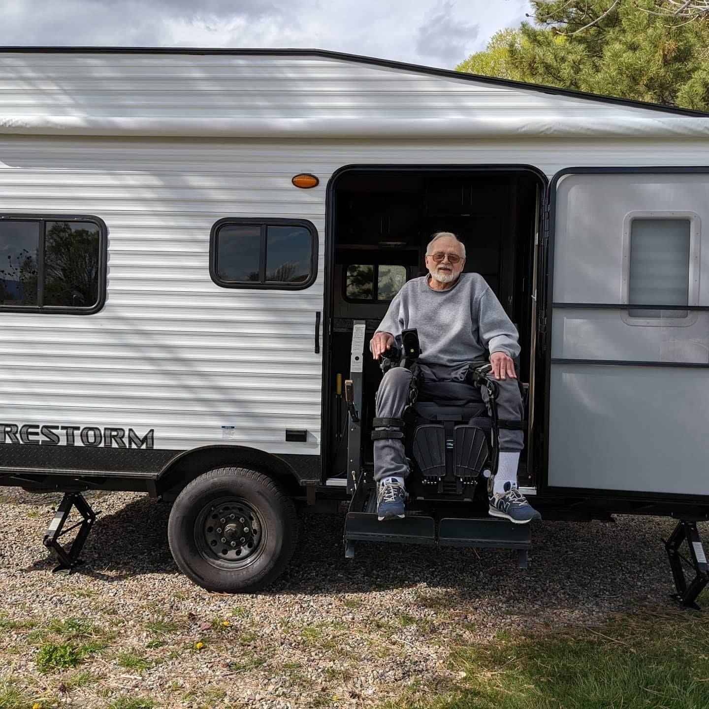 Man in wheelchair in doorway of RV, step down, gravel driveway.