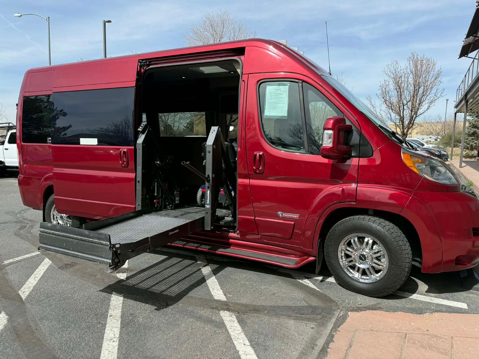 Person in wheelchair using a ramp to enter a white accessible van on a sunny day.
