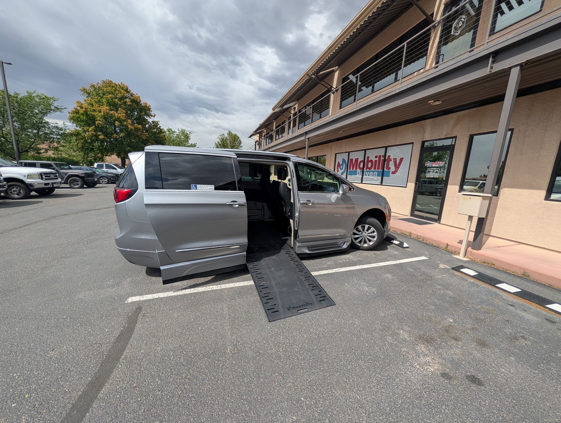 Silver wheelchair-accessible van with ramp deployed in a parking lot