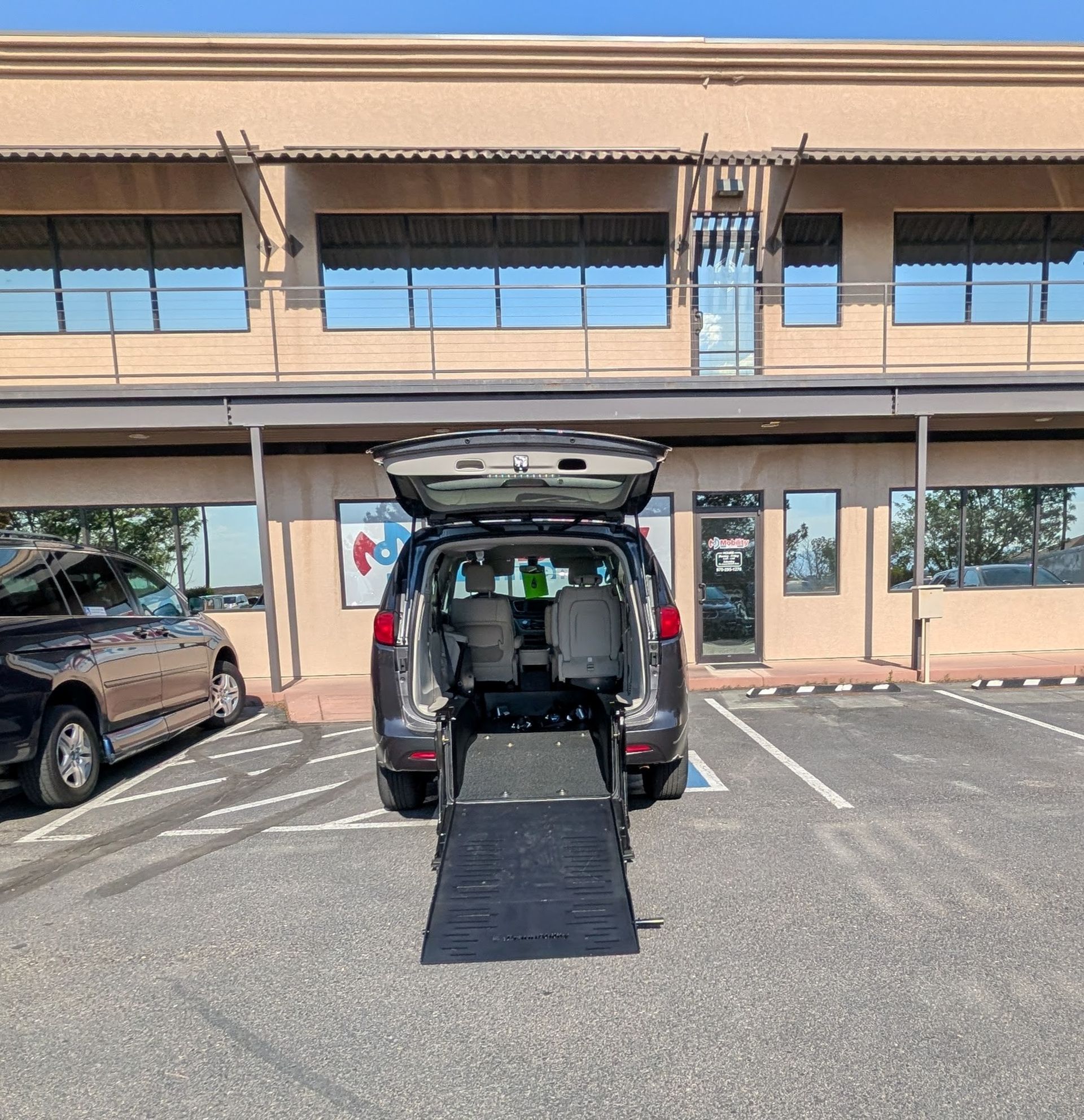 Person in wheelchair using a ramp to enter a white accessible van on a sunny day.