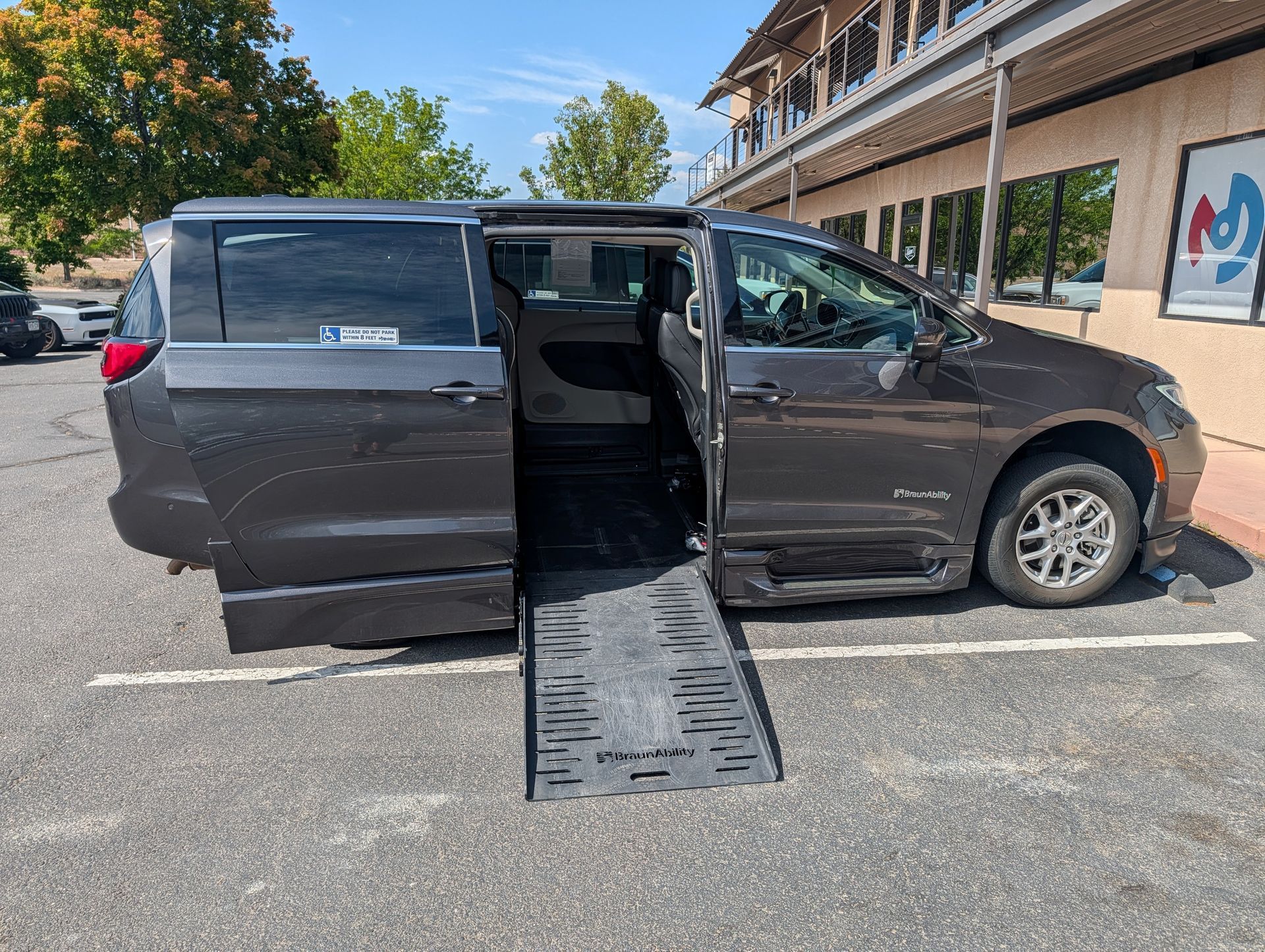 Person in wheelchair using a ramp to enter a white accessible van on a sunny day.