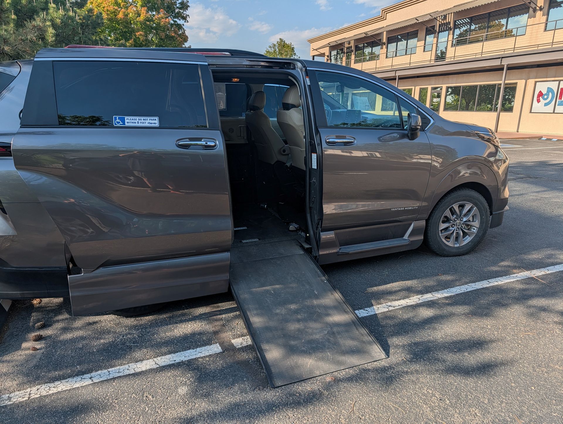 Person in wheelchair using a ramp to enter a white accessible van on a sunny day.