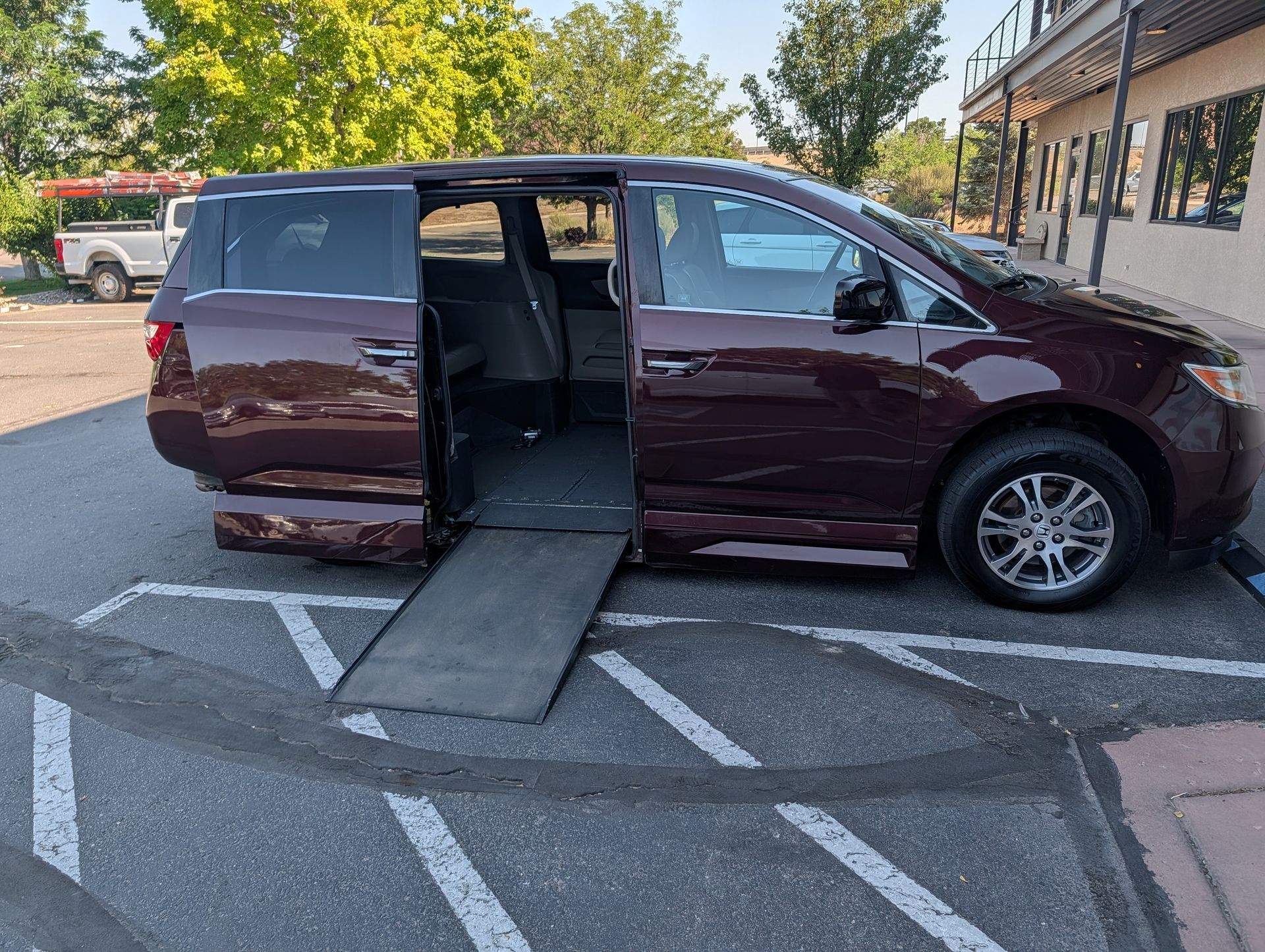 Maroon minivan with side ramp deployed in a parking lot, likely for wheelchair access