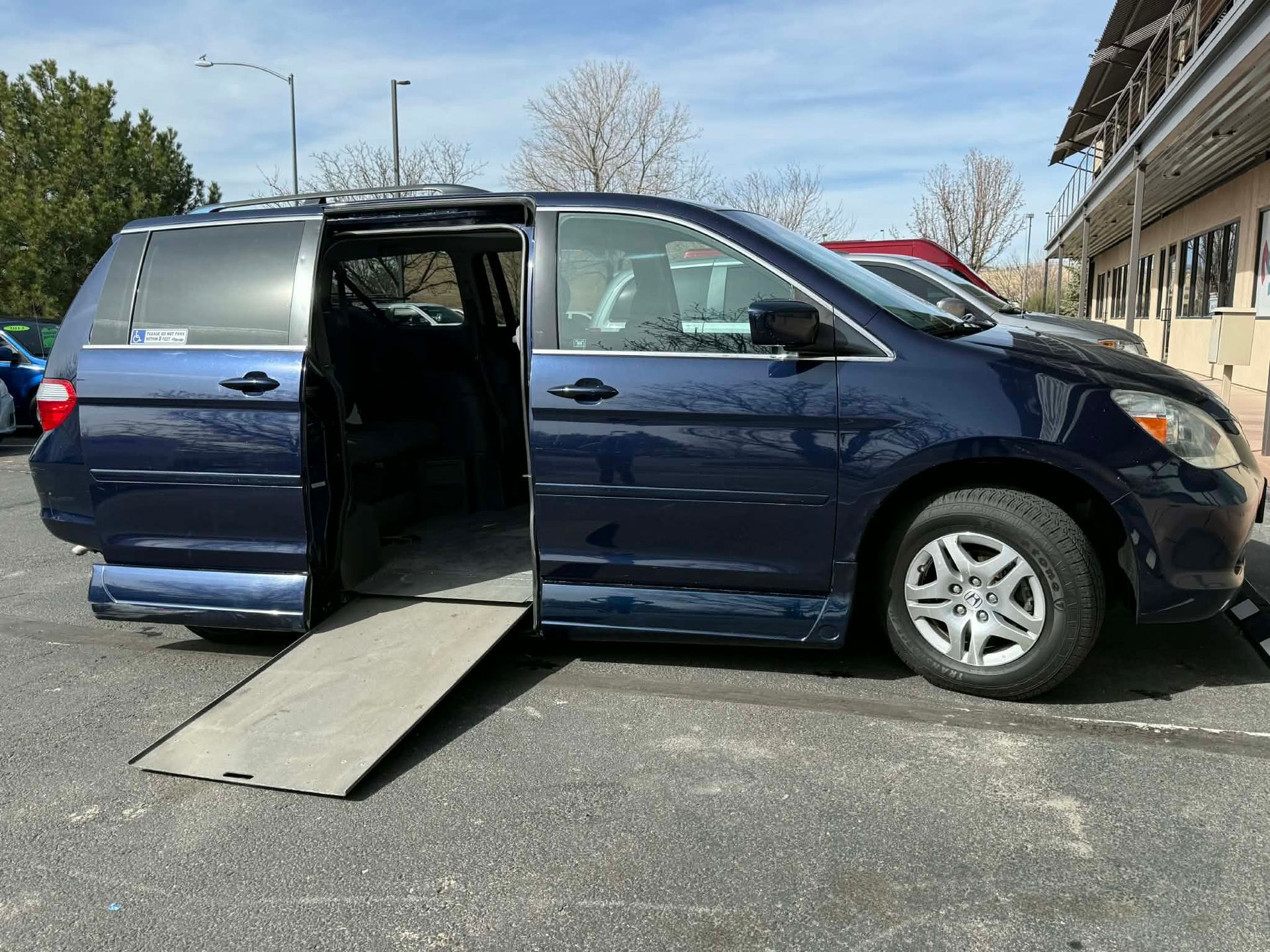 Person in wheelchair using a ramp to enter a white accessible van on a sunny day.