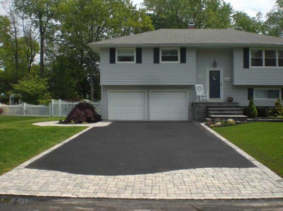 A split-level home with a newly paved asphalt driveway featuring a decorative stone border and entry apron.