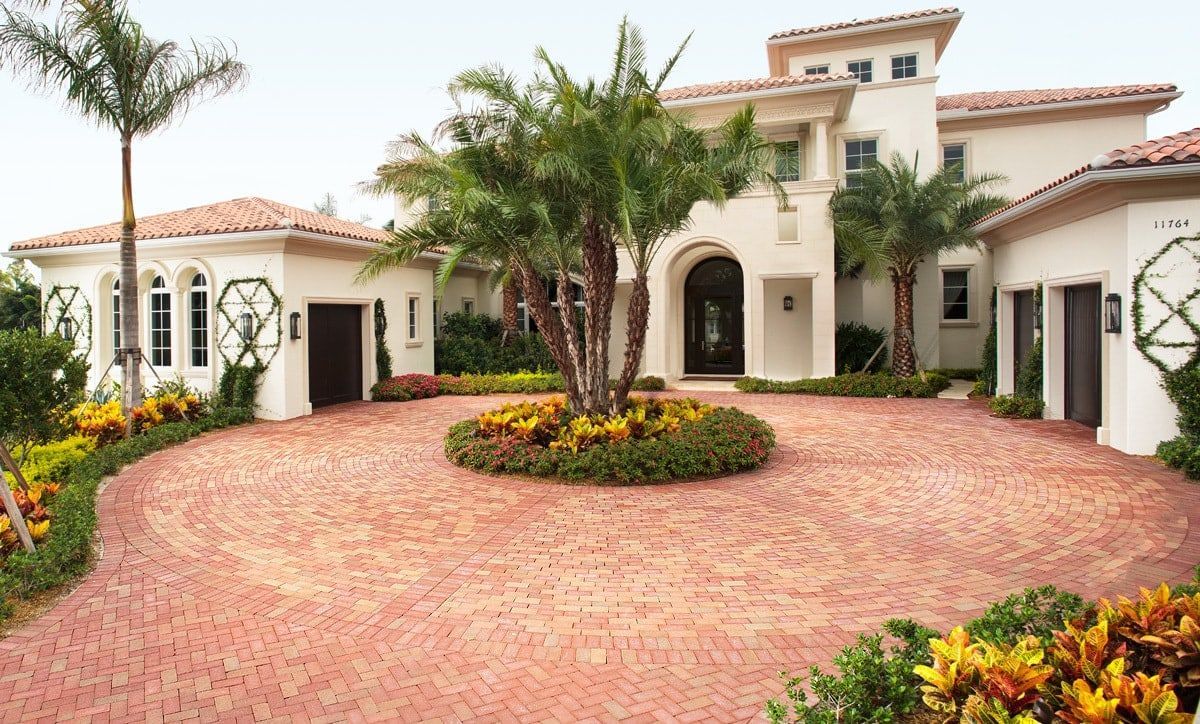 A Mediterranean-style house with a cream stucco exterior, red tile roof, and a large, circular brick driveway.
