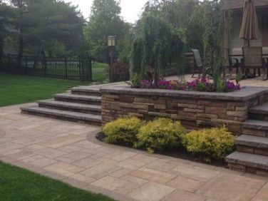 Stone patio steps leading to a raised garden bed with purple flowers and shrubs in a landscaped backyard.