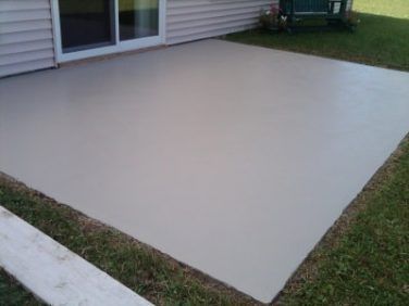 A light gray, smooth concrete patio adjacent to a house with beige siding and a sliding glass door.