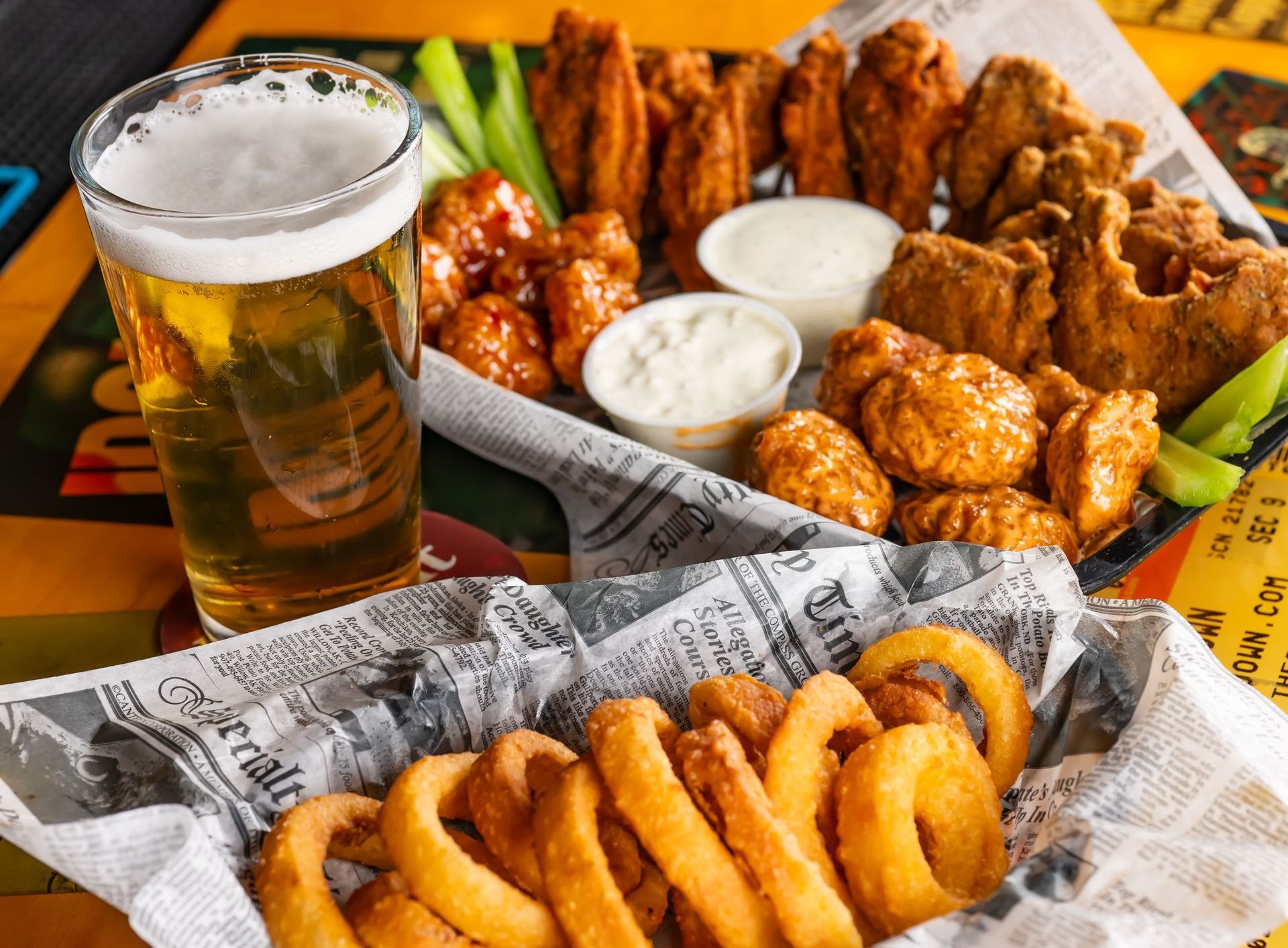 A basket of onion rings , chicken wings , and a glass of beer on a table.