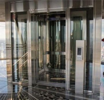 Glass revolving door entrance with metal frames and a wall-mounted access panel