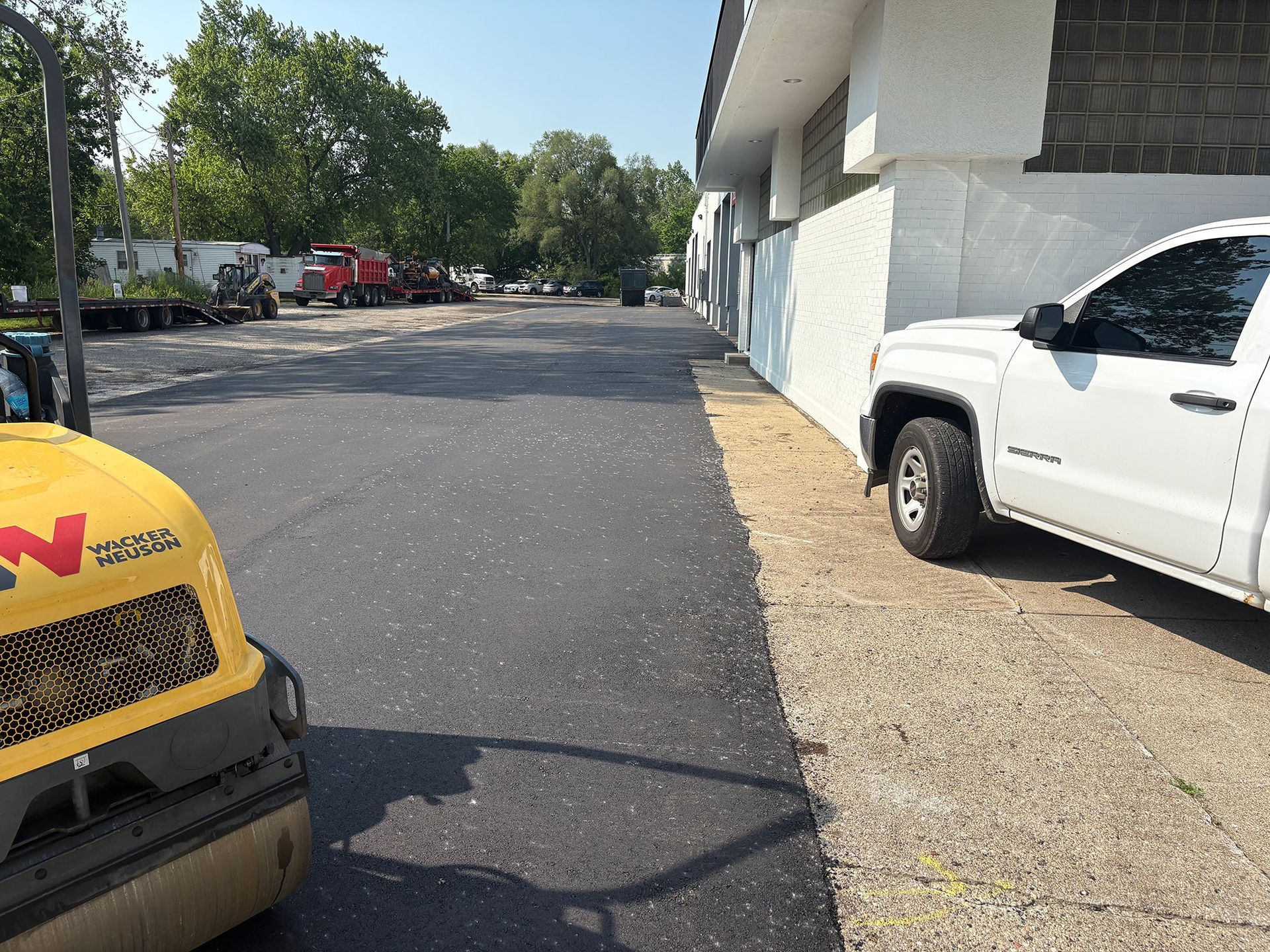 A white truck is parked on the side of the road next to a yellow roller.