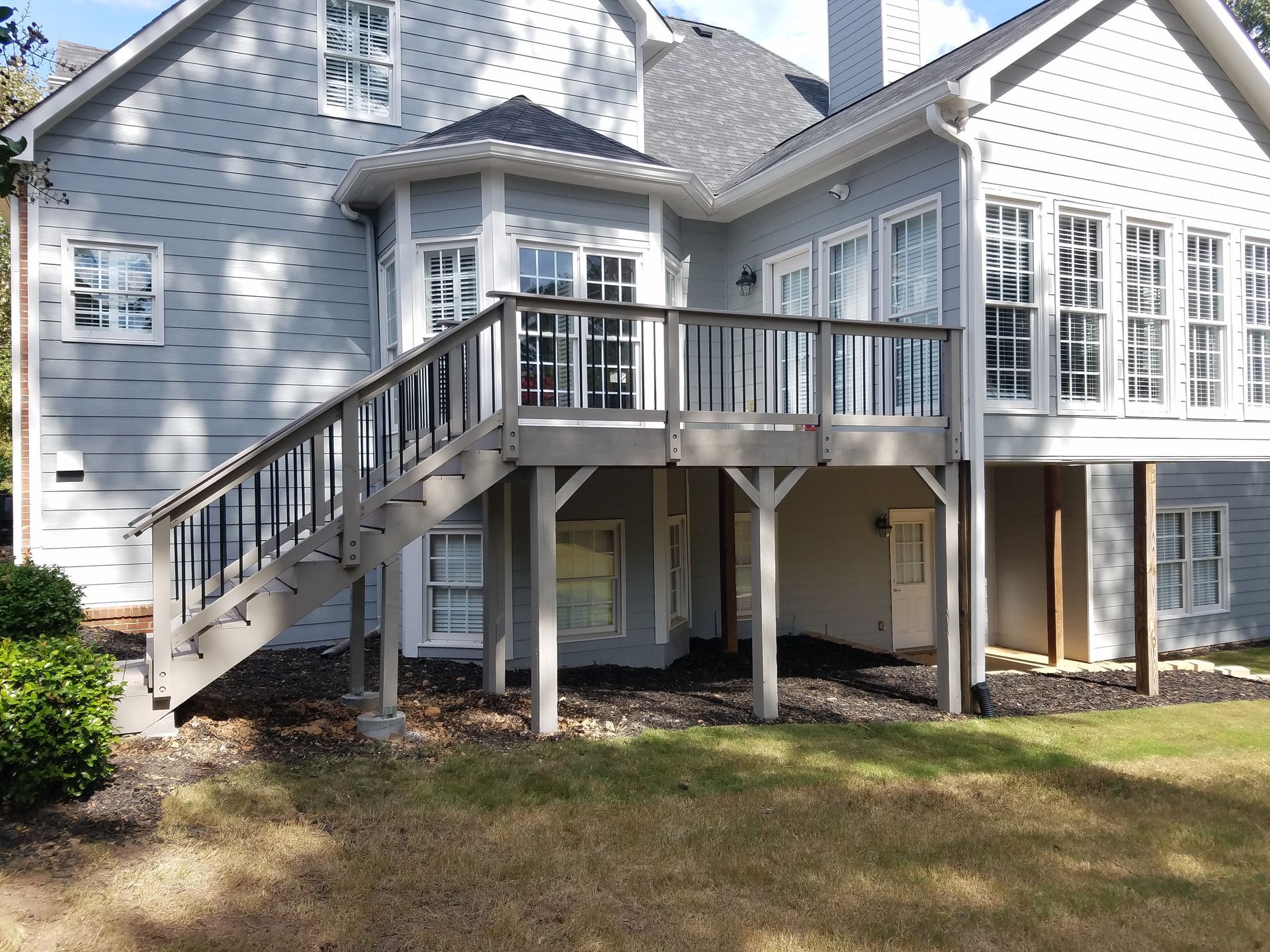 Gray house with deck, dark handrails, and steps leading down to yard.