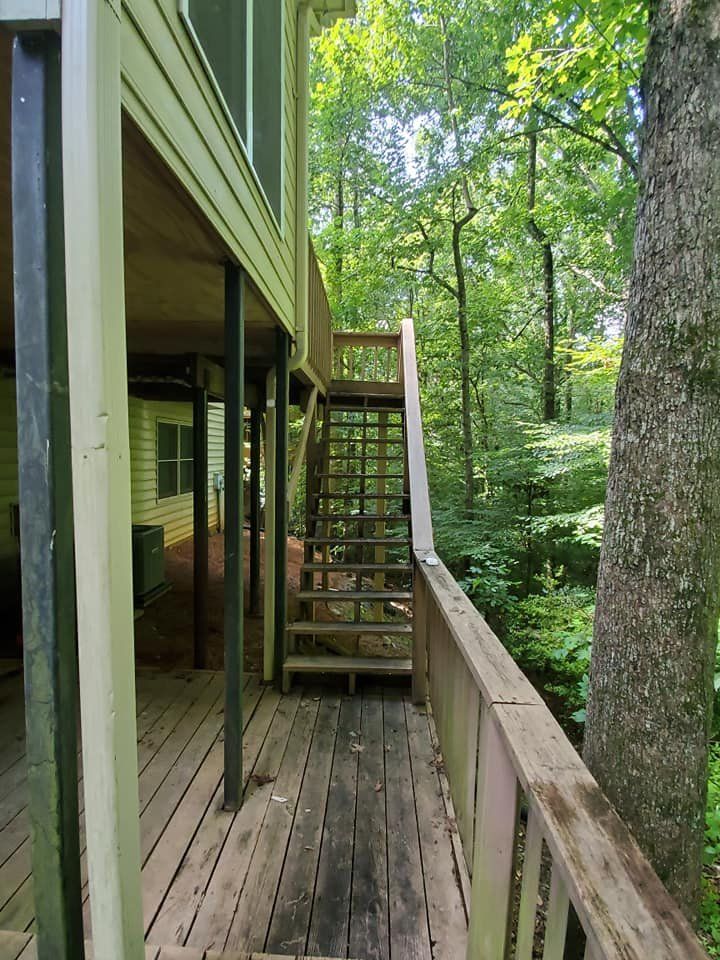 Wooden deck with exterior stairs leading up to a porch, surrounded by trees.