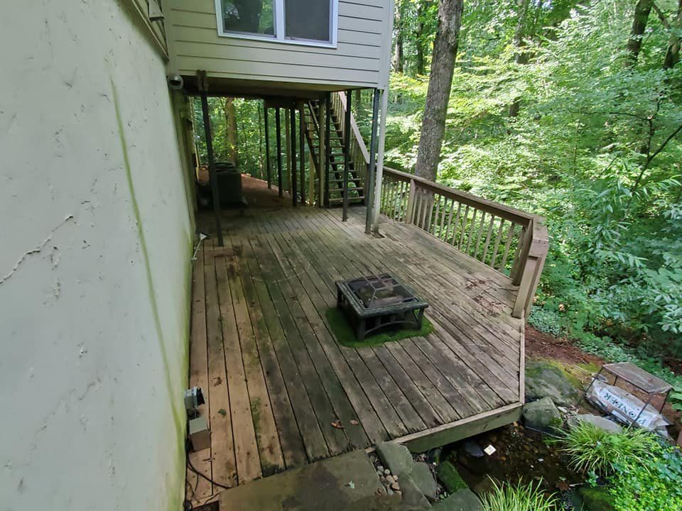 Wooden deck with fire pit, next to a house and surrounded by trees.
