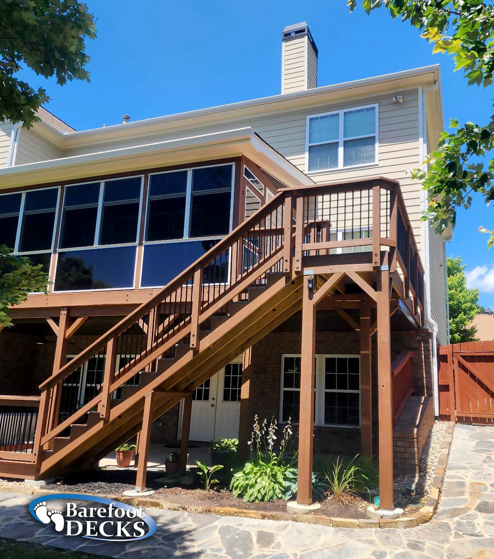 Two-story house with a wooden deck and enclosed porch, featuring dark-tinted windows. Sunny day.