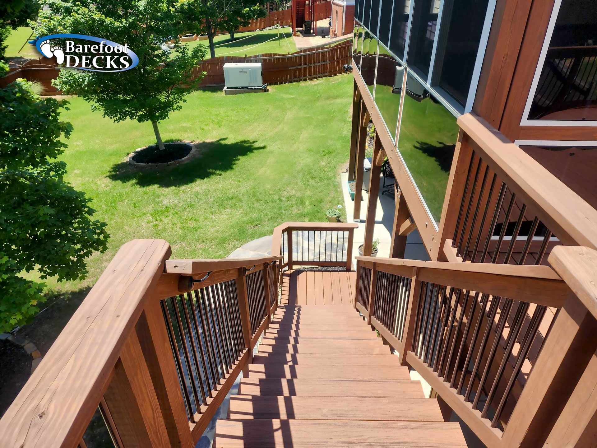 Wooden deck with stairs leading to a green yard. Brown railings and stairs.