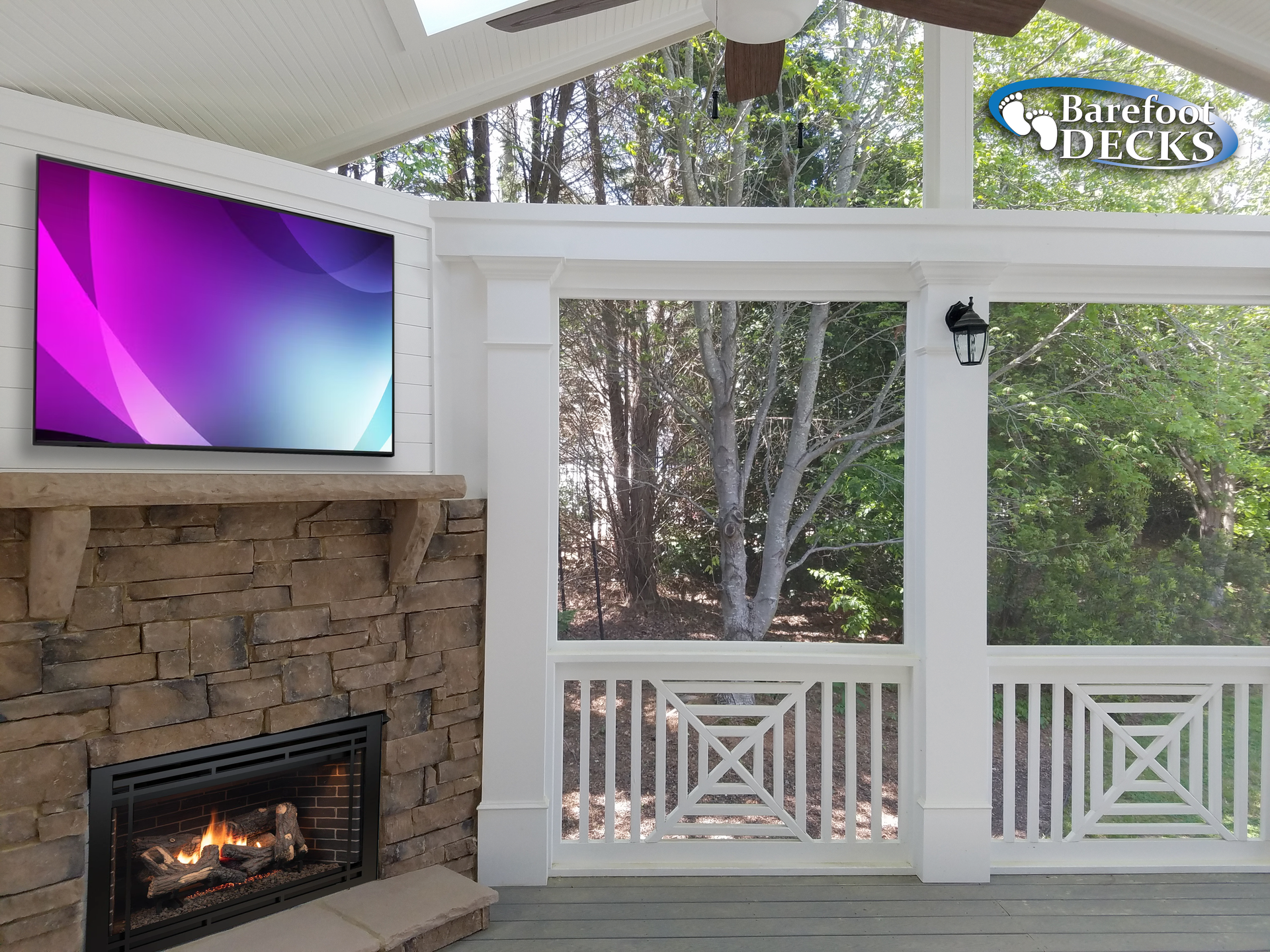 Outdoor porch with a fireplace, TV, and view of trees. White columns and decorative railing.