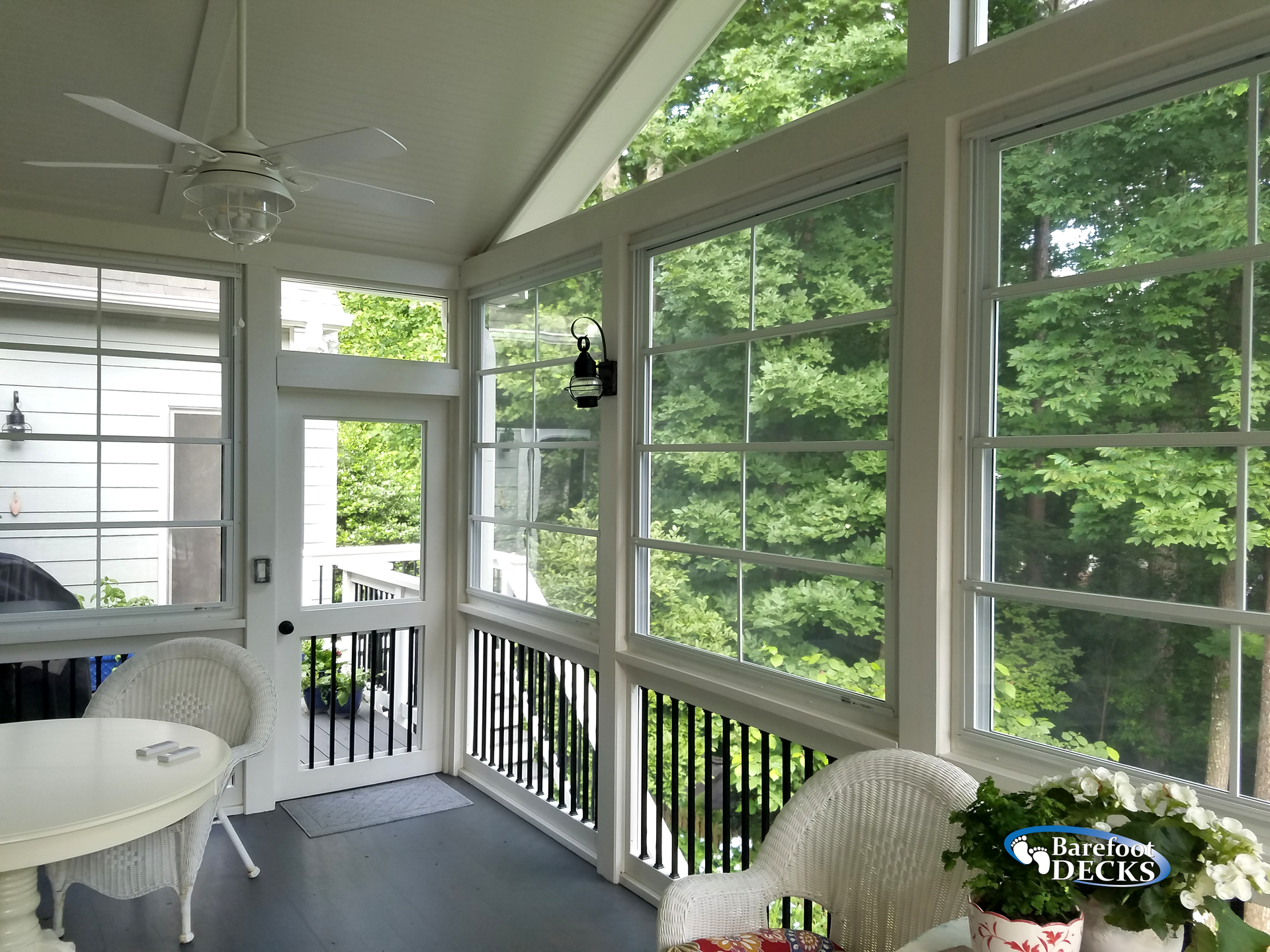 Screened porch with white trim, wicker furniture, and large windows looking out at green trees.