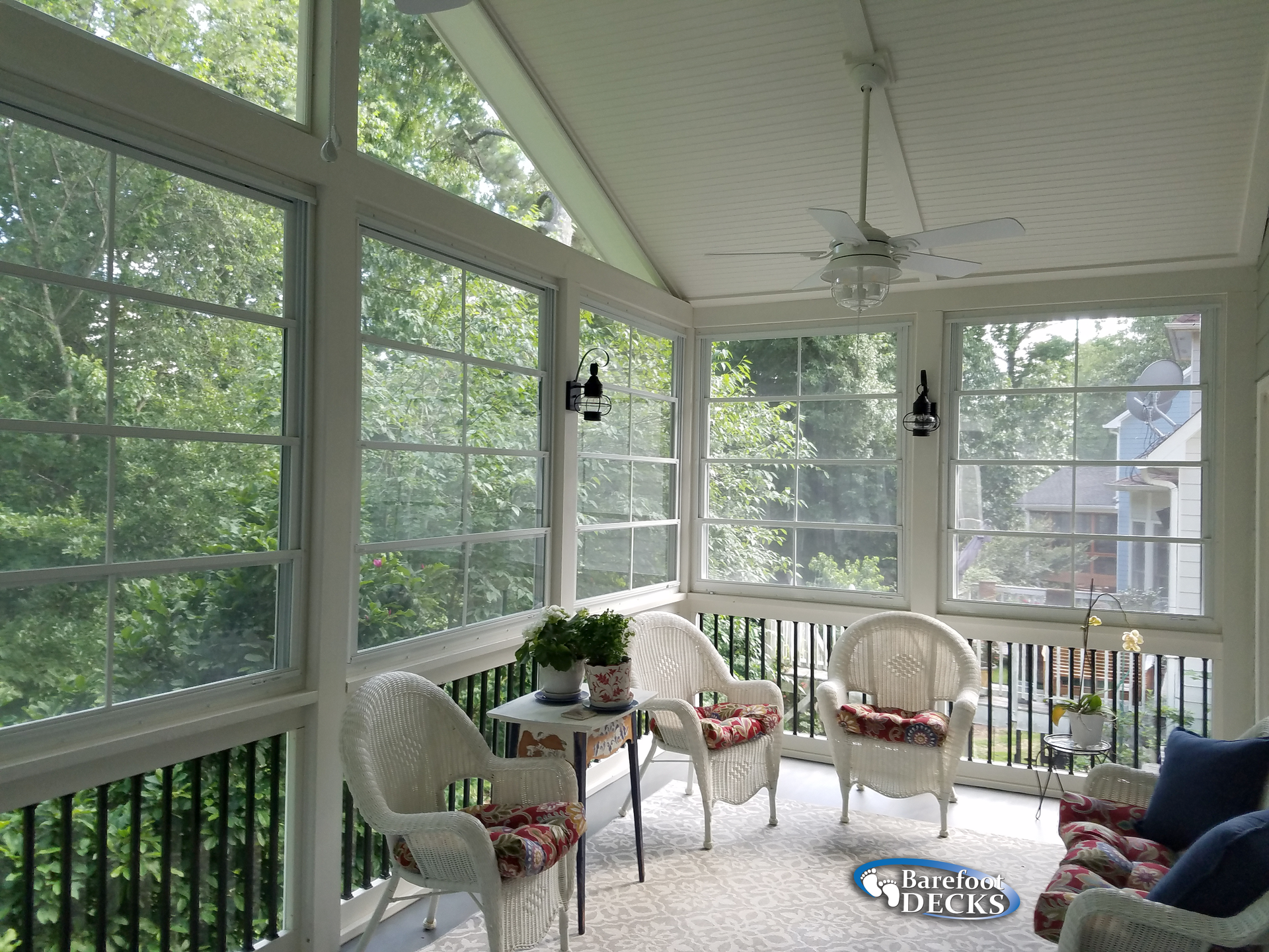 Sunroom with wicker furniture, windows overlooking lush greenery.